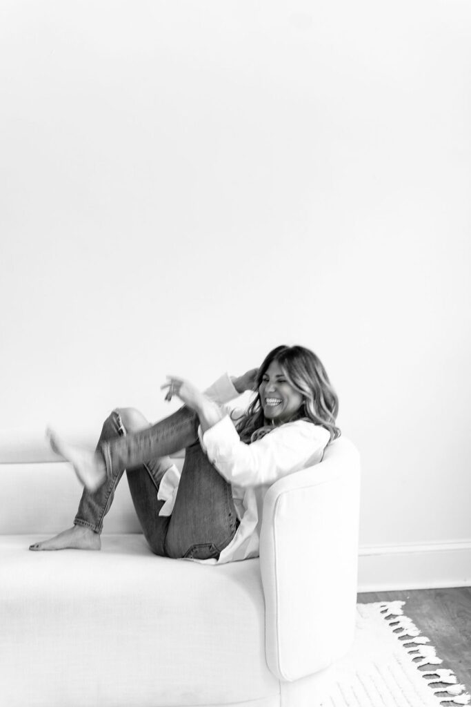 Andrea Kind laughing and reclining on a white sofa, embodying joy and relaxation
