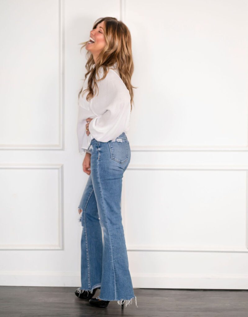 Andrea Kind smiling while standing in a relaxed pose wearing a white shirt and blue jeans.